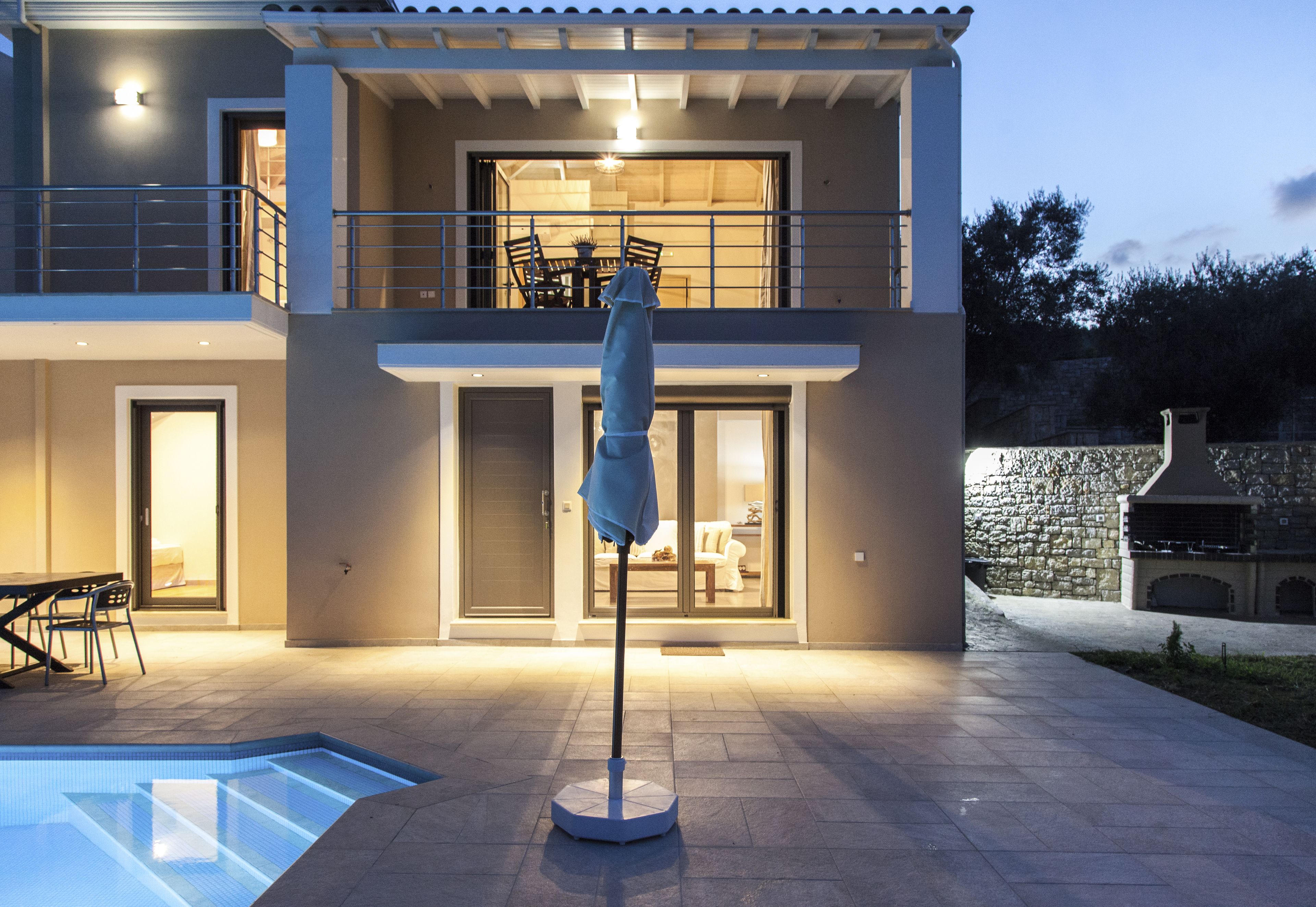 A modern two-story house with a swimming pool, outdoor seating, and a stone wall.