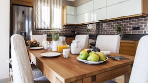 A modern kitchen with a wooden dining table set for breakfast, including fruits, a pitcher of orange juice, and a coffee maker. - Alivia Lefkas (Lefkada)