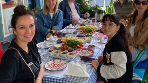 A group of people dining at an outdoor table with a blue and white checkered tablecloth, surrounded by potted plants and flowers. - Incitta Otel (Seferihisar)