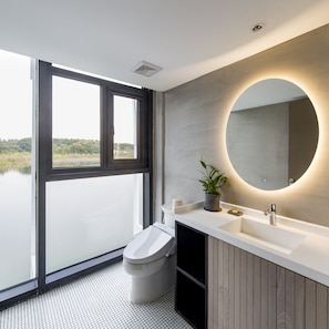 Un baño moderno con un ventanal grande, un espejo redondo y un lavamanos.