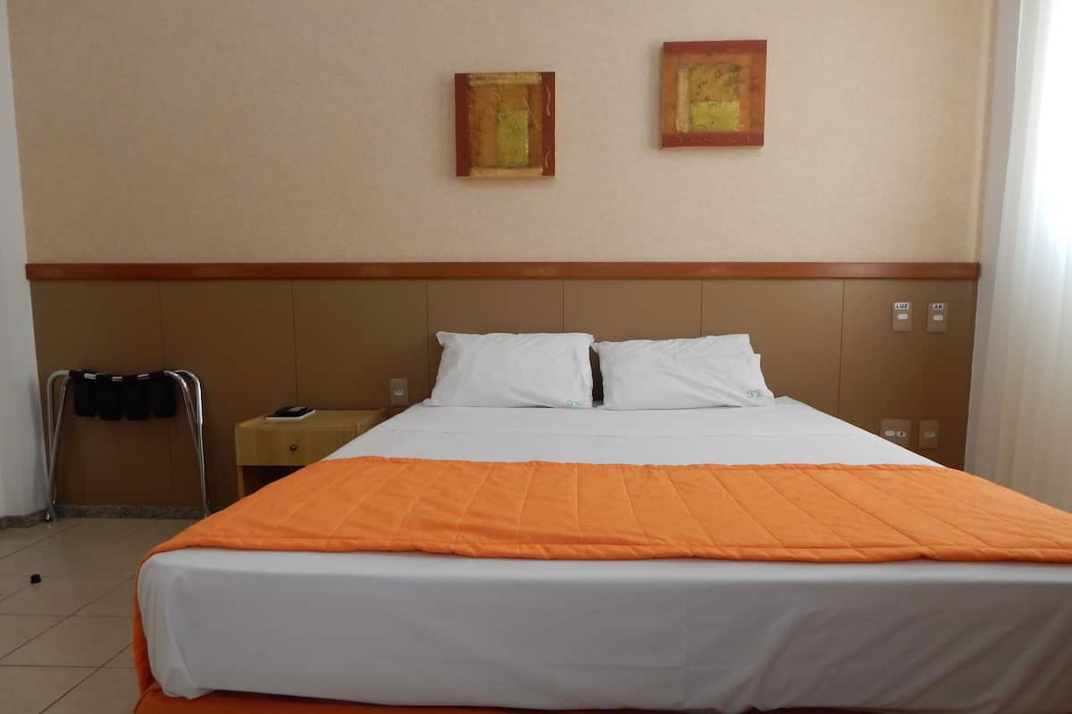 Une chambre d’hôtel avec un lit, deux oreillers, une table de chevet, une lampe et deux tableaux au mur.