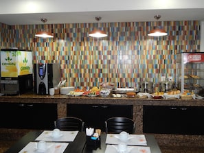 A breakfast buffet area with a colorful tile backsplash, a coffee machine, and a variety of food options. - Frimas Hotel (Belo Horizonte)