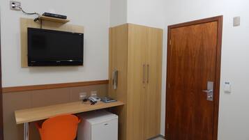 Une petite pièce avec un bureau en bois, un téléviseur fixé au mur, une armoire et une porte.