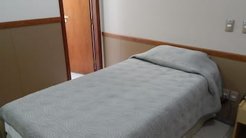 A small, neatly made bed with a patterned bedspread in a room with wooden paneling and a tiled floor.