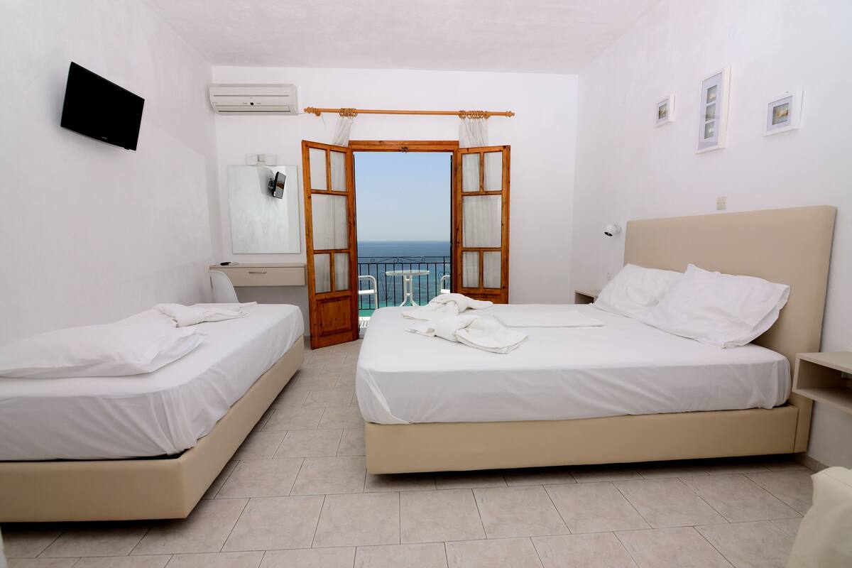 A hotel room with two beds, a TV, a balcony with a view, and a wooden door.