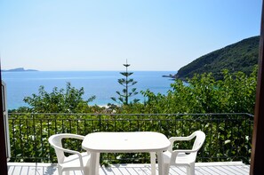 Ein Balkon mit weißem Tisch und zwei Stühlen, der auf ein Gewässer und eine hügelige Landschaft blickt.