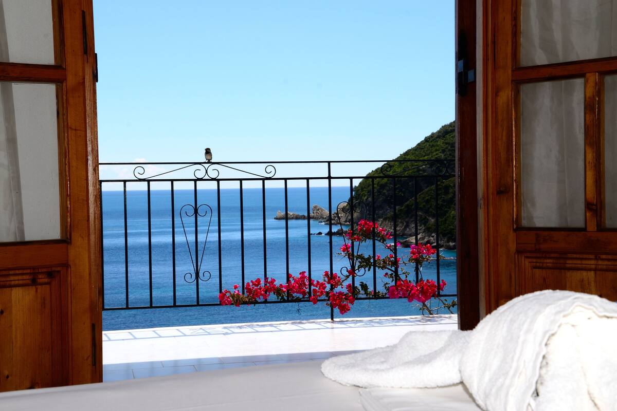 A balcony with a view of the sea, a wooden door, and a white towel on the floor.