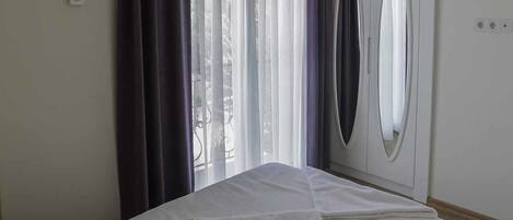 A hotel room with a bed, a window with curtains, a wardrobe, and a wall-mounted air conditioning unit.