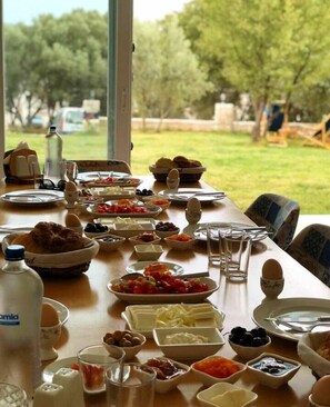 A dining table set outdoors with various dishes, glasses, and a bottle of water. - Clementine Suits Sigacik (Seferihisar)