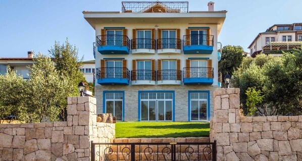 A multi-story building with balconies, stone walls, and a well-maintained lawn.