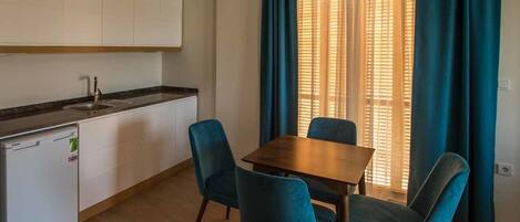 A compact kitchen with a sink, a small refrigerator, and a dining table with four chairs.