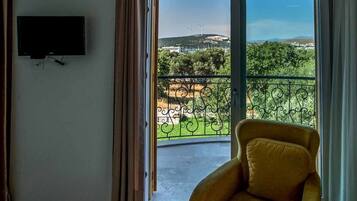 A room with a large sliding glass door leading to a balcony with a view of wind turbines and greenery.