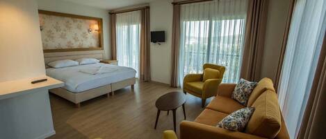 A hotel room with a bed, a sofa, a chair, a small table, and a TV.