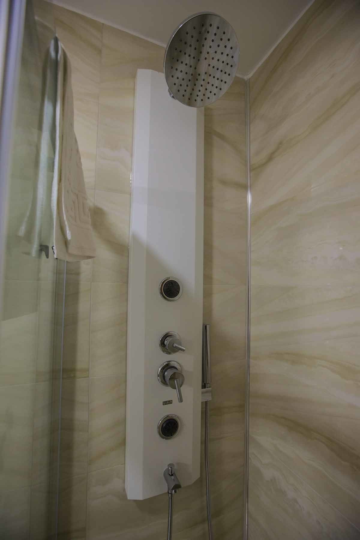 A modern shower enclosure with a control panel, a handheld showerhead, and a glass door.
