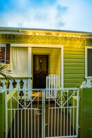 Una casa verde con un portón blanco, una puerta de madera y luces colgantes.