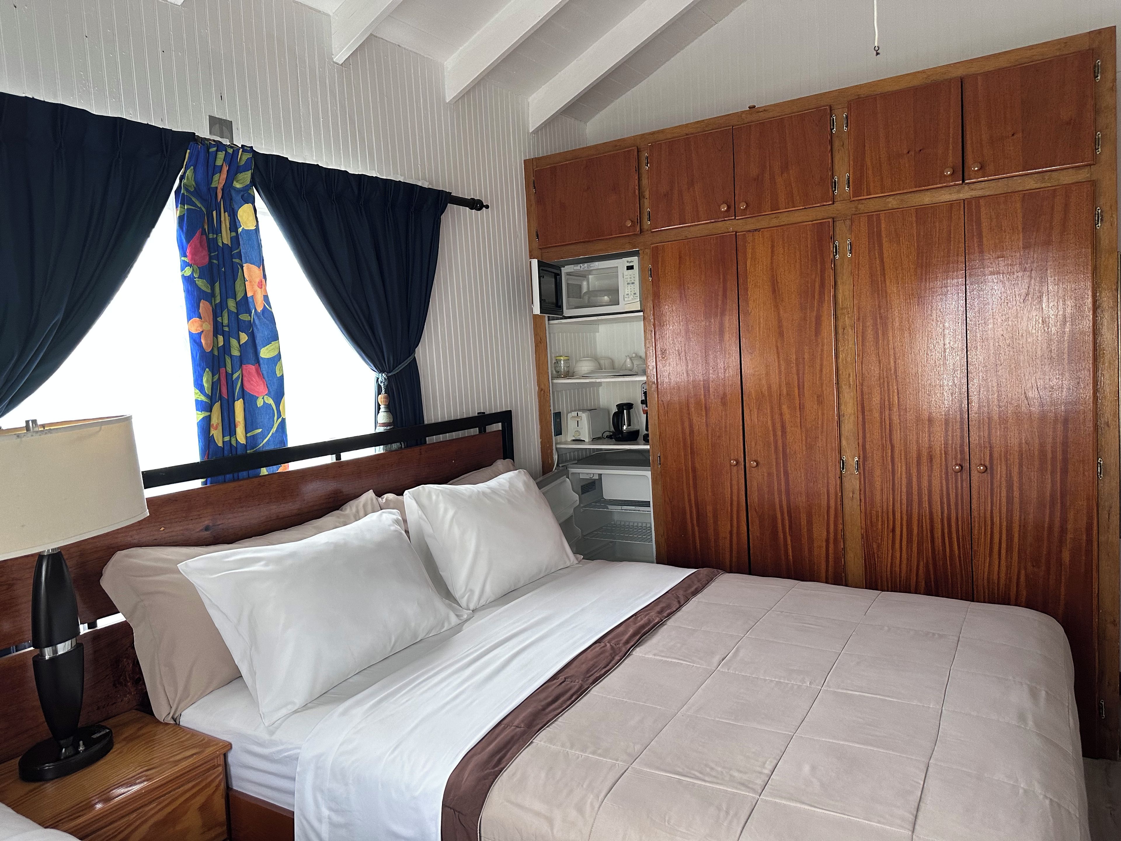 A hotel room with a bed, wooden wardrobe, and a kitchenette.