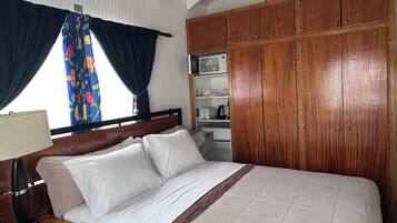 A hotel room with a bed, wooden wardrobe, and a kitchenette.