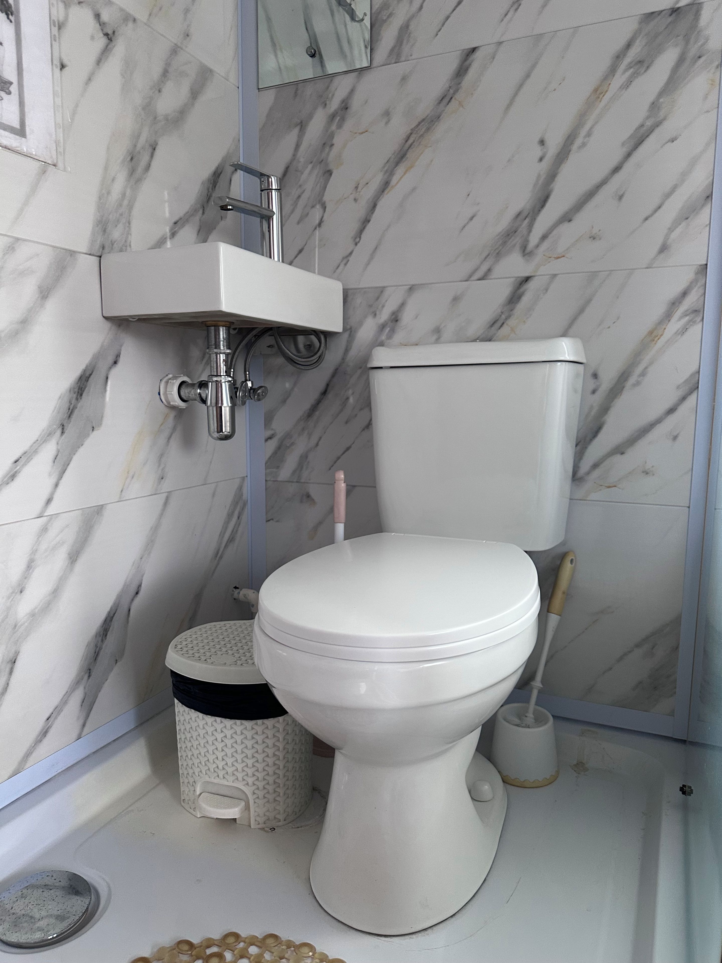 Un baño con inodoro blanco, lavamanos instalado en la pared y un escobillón para inodoro.