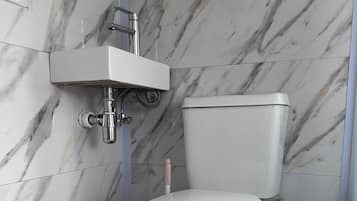 Un baño con inodoro blanco, lavamanos instalado en la pared y un escobillón para inodoro.
