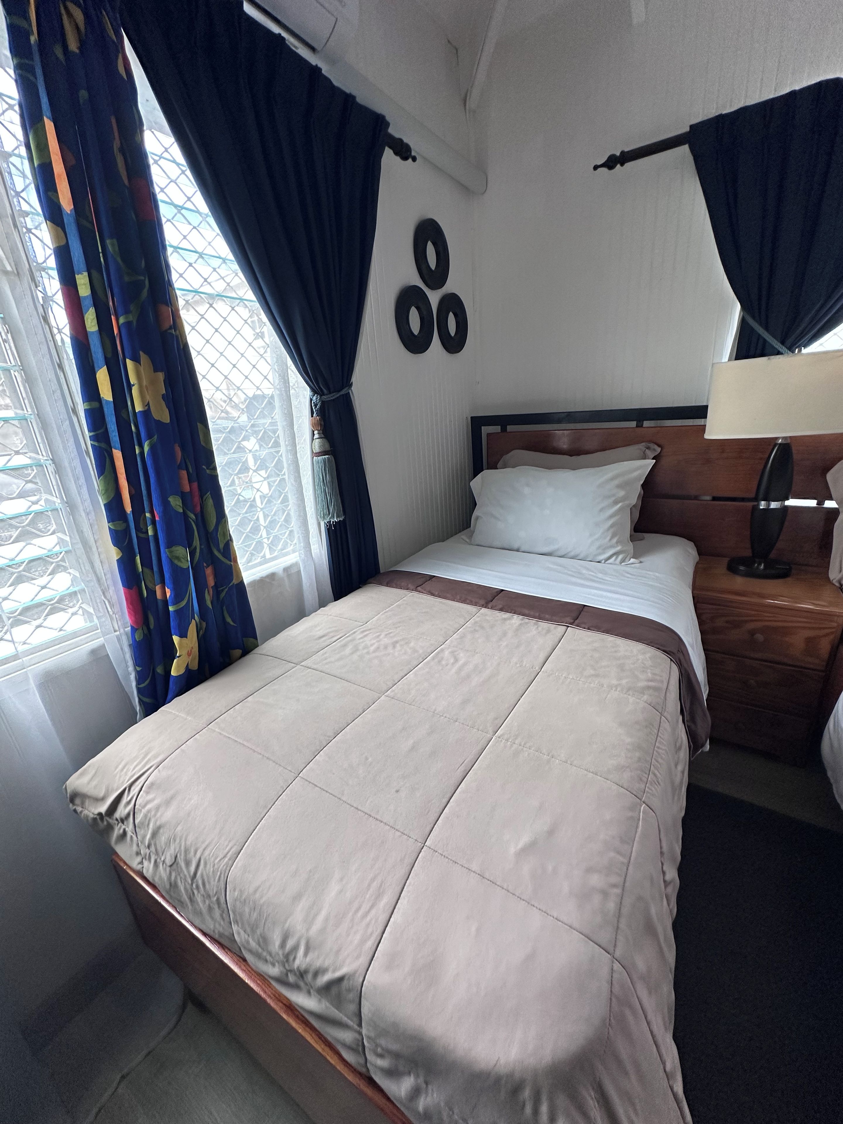 Una habitación de hotel con cama, mesita de noche, lámpara y ventana con cortinas.