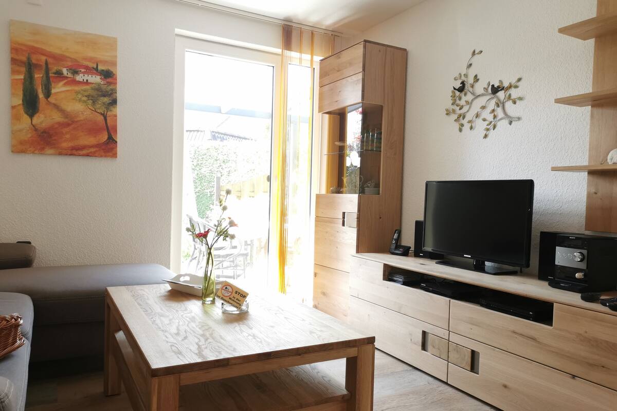 Ein modernes Wohnzimmer mit einem Holzespeisetisch, einer Couch, einem Fernseher und einer Küchenzeile mit Holzschränken.