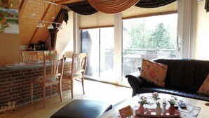 Un salon chaleureux avec un plafond en bois, un canapé en cuir noir, un coin repas avec des chaises en bois et une cuisine avec un mur en briques et des placards en bois.
