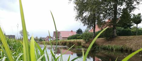 A calm water body with surrounding greenery and a distant building with a red roof.