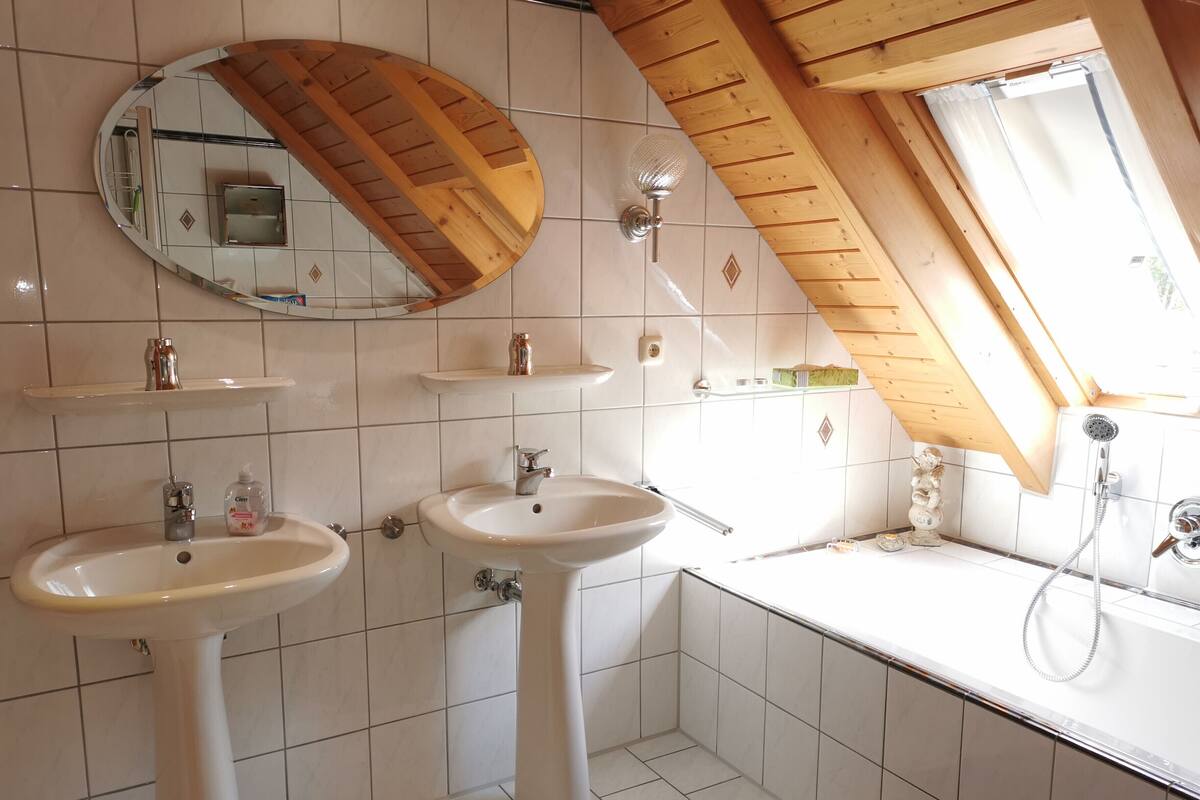 Ein Badezimmer mit zwei Waschbecken, einem Spiegel, einer Dusche und einem Dachfenster.