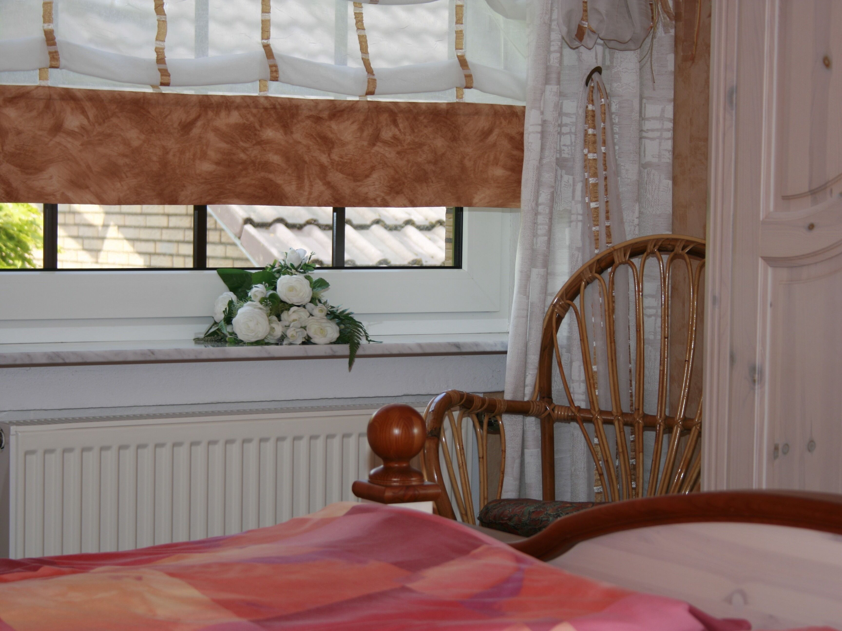 A bedroom with a bed, a chair, a window with curtains, and a radiator.
