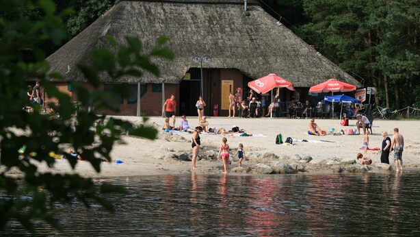 Une plage avec un bâtiment à toit de chaume, des gens qui se détendent et des parasols.