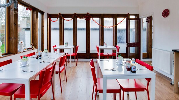 Un comedor con mesas blancas y sillas rojas, ventanas amplias con vidrio esmerilado y vistas a una masa de agua.