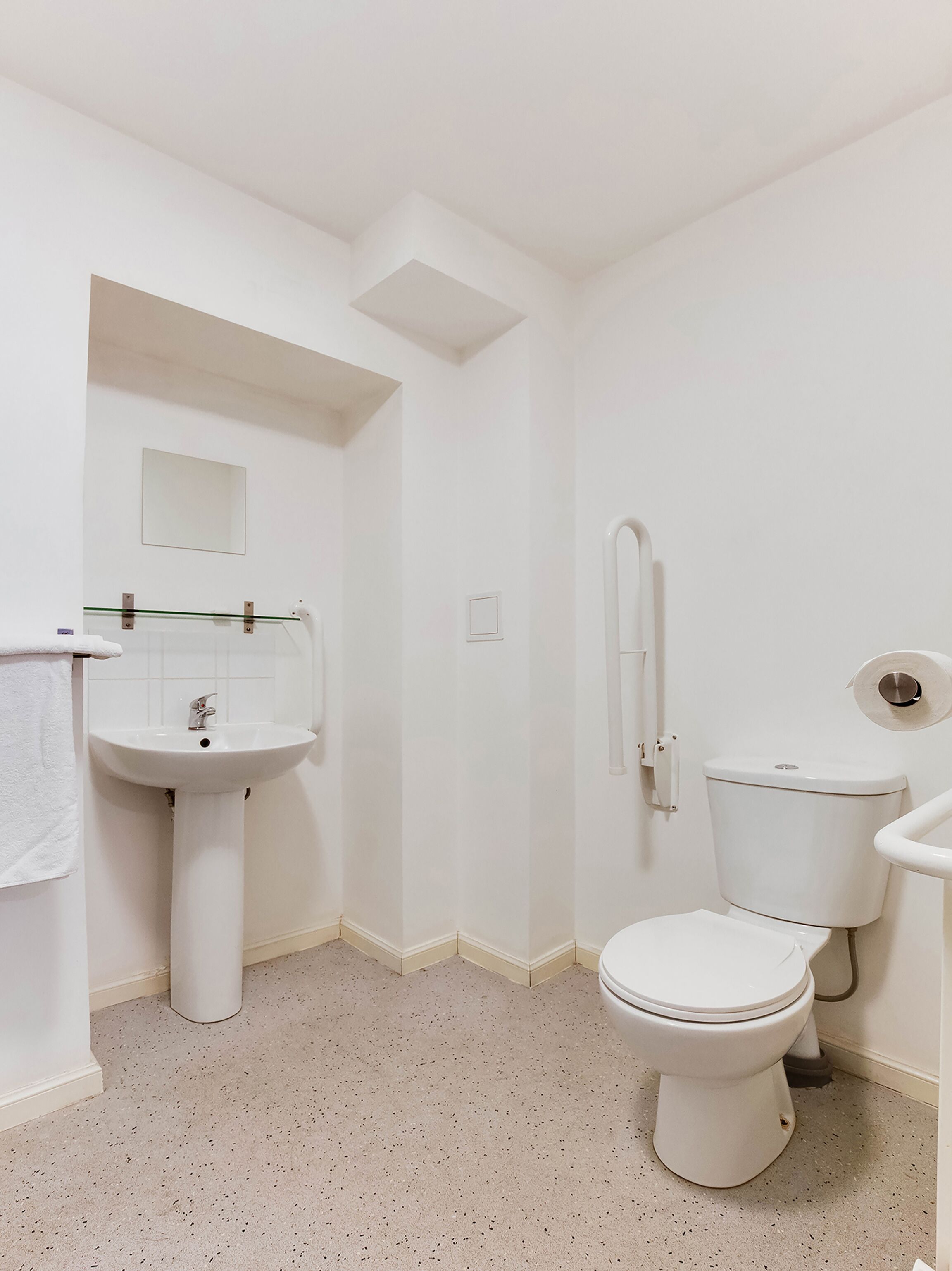 A small, white bathroom with a pedestal sink, a toilet, and a shower area.