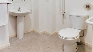 A small, white bathroom with a pedestal sink, a toilet, and a shower area.