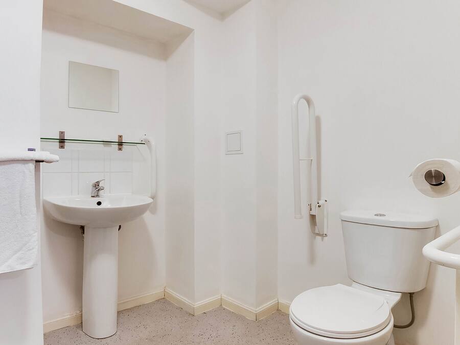 A small, white bathroom with a pedestal sink, a toilet, and a shower area.