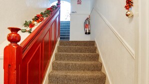 Una escalera con alfombra y barandilla roja que lleva a un rellano con extintor y un cartel de prohibido fumar.