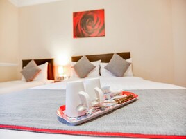 A neatly made bed with pillows, a tray with a cup and a spoon, and a red and white tray.
