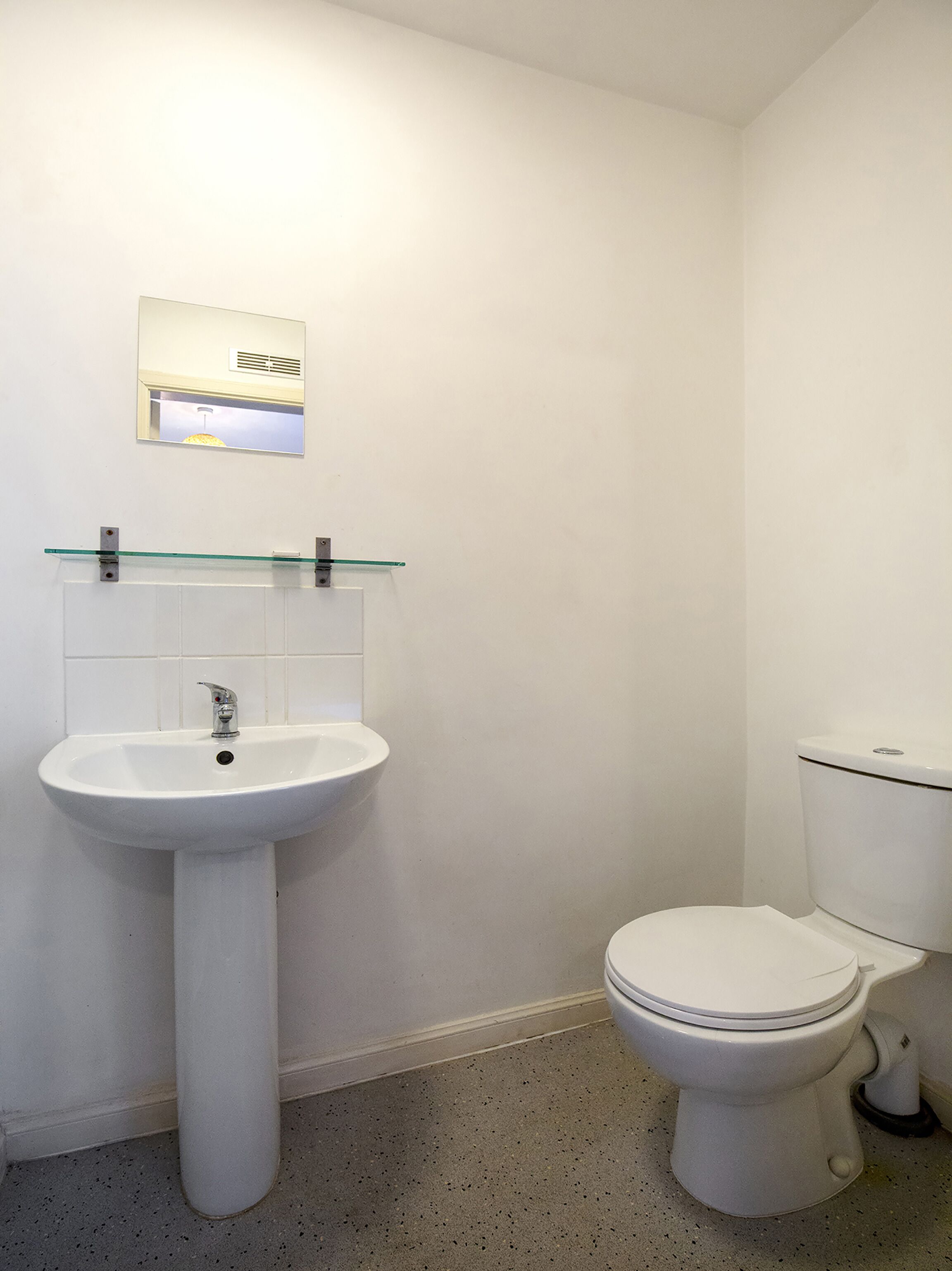 A bathroom with a white sink, a glass shelf above it, and a toilet.