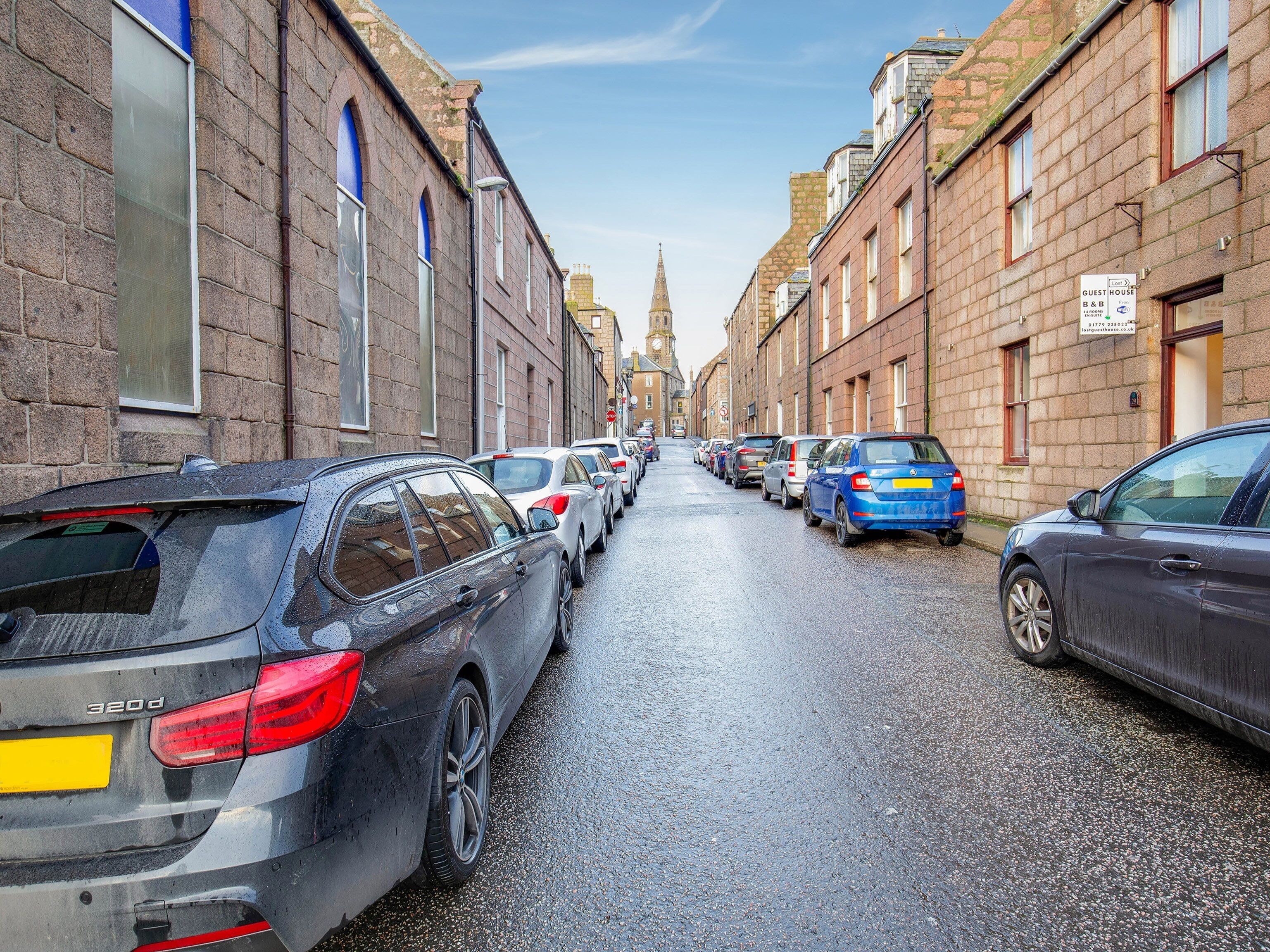 A narrow street lined with parked cars and historic buildings.