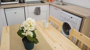 A small kitchenette with a microwave, coffee maker, and fruit basket. There is a washing machine and a table with a potted plant and a mug.