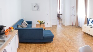 A modern living room with a sofa, a coffee machine, a fruit basket, and a TV.