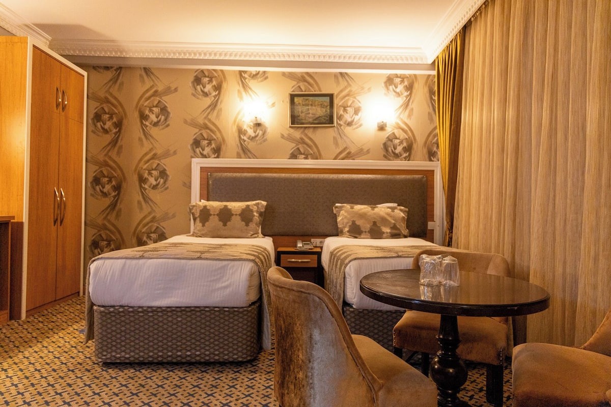 A hotel room with two beds, a small table, and a sofa.