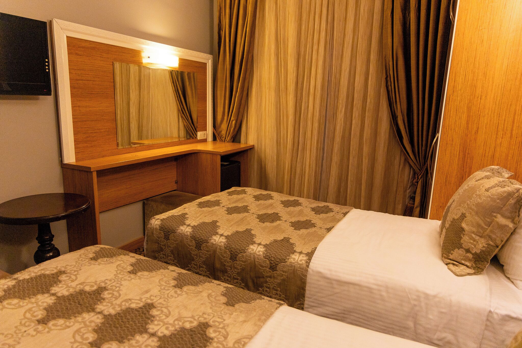 A hotel room with two beds, a wooden headboard, a small table, and a television.