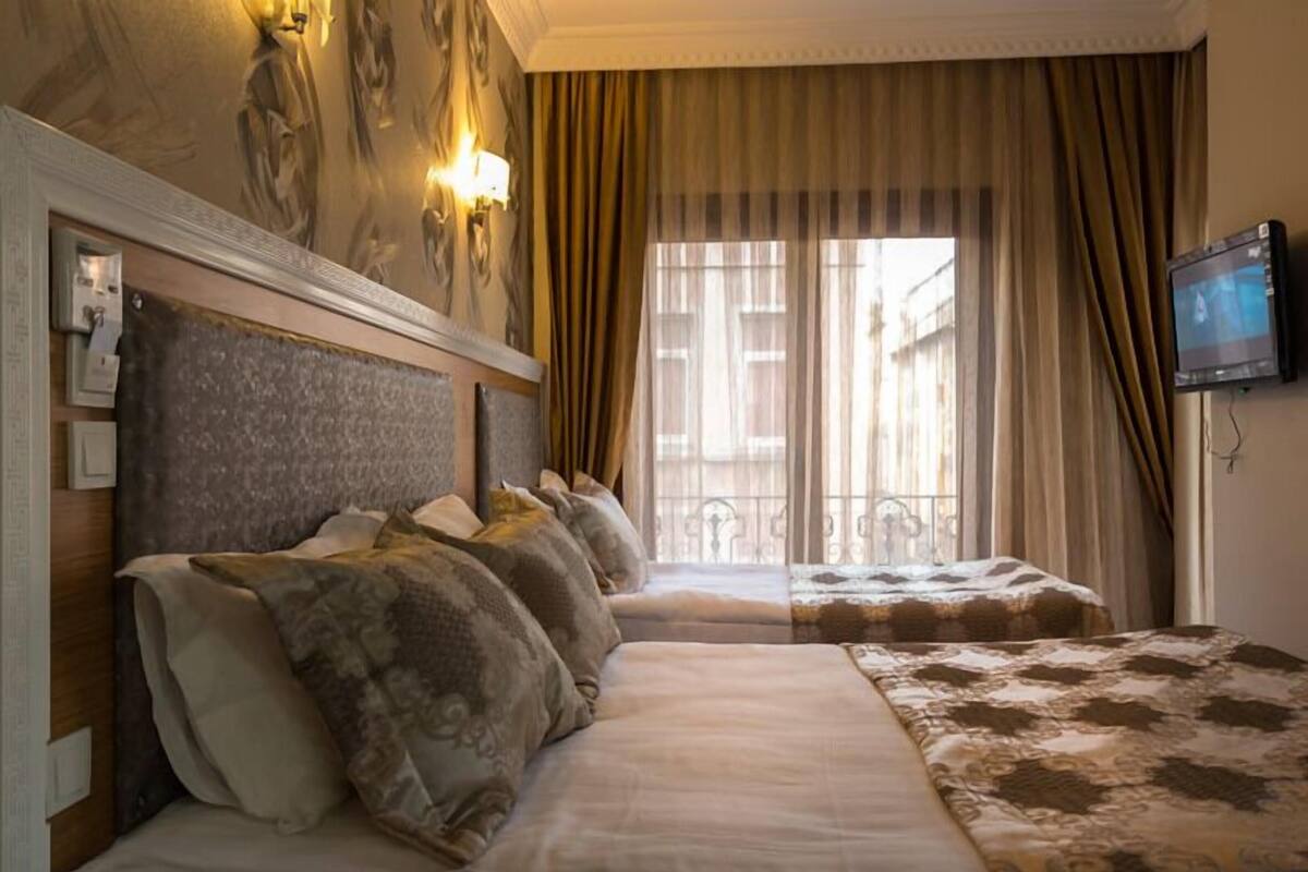 A hotel room with two beds, a television, and a view of the city through large windows.