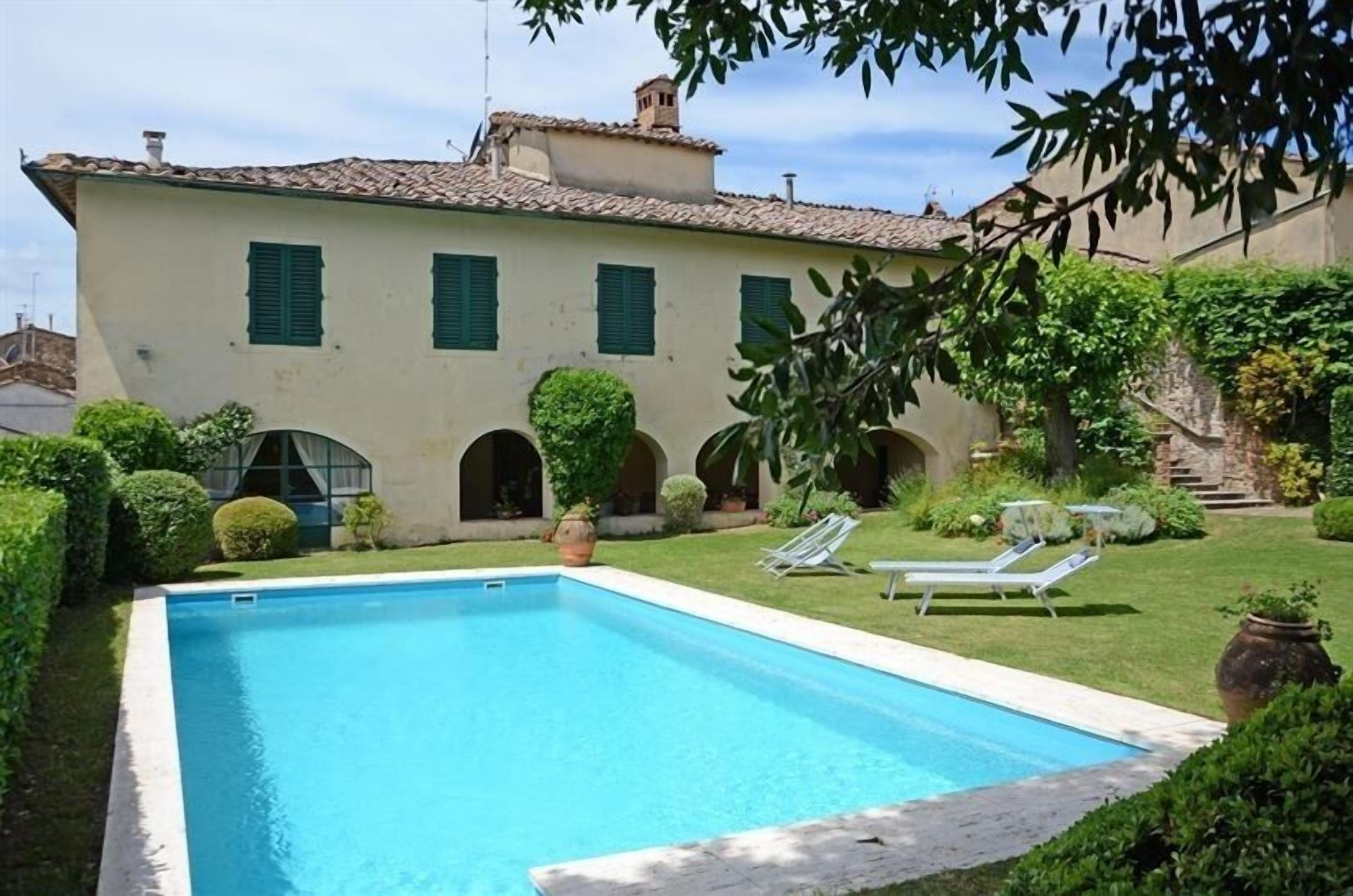 A swimming pool with a clear blue water, surrounded by a well-maintained lawn and a building with green shutters.