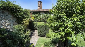Un muro de piedra, un jardín con un sendero y un edificio con una torre campanario.