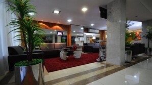 Un hall d’entrée moderne avec un tapis rouge, une grande plante en pot, un canapé et un téléviseur.