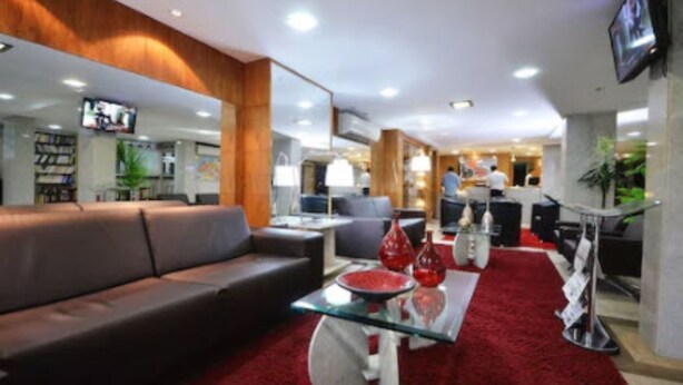 Un hall d’hôtel moderne avec un tapis rouge, un canapé, une table basse en verre et un téléviseur fixé au mur.