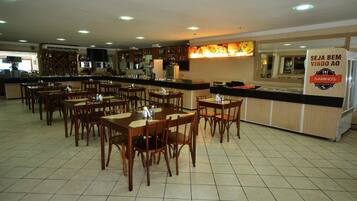 A restaurant with multiple dining tables and chairs, a bar area, and a kitchen in the background.