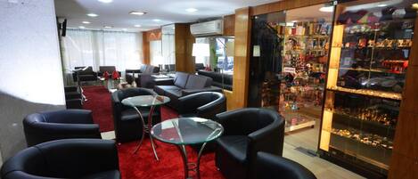 A hotel lobby with leather sofas, glass tables, a red carpet, and a glass display case with souvenirs.