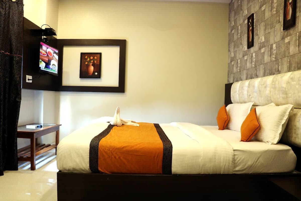 A neatly made bed with a white and orange bedspread, a small bedside table with a book, and a television mounted on the wall.